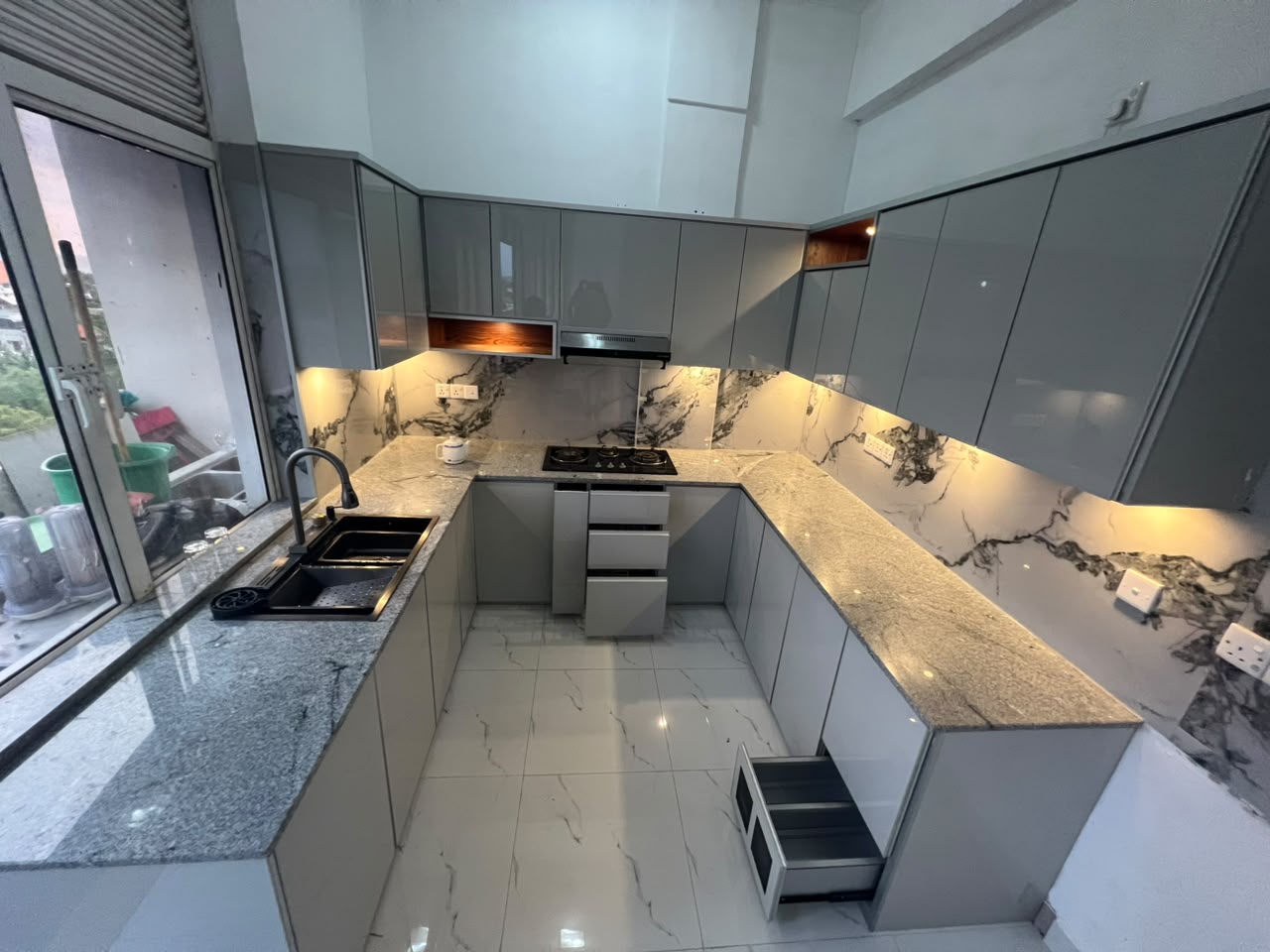 Grey U-shaped kitchen with marble backsplash and warm lighting